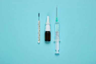 Mavi arka planda tıbbi hayat. Şırınga, termometre, burun spreyi. Minimalizm