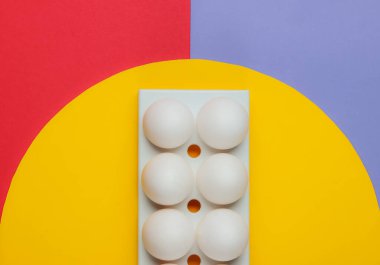 Renkli arka planda beyaz tavuk yumurtaları ve ortasında sarı daire olan bir tepsi. Minimalist gıda konsepti.
