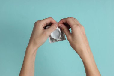 Kadın eli mavi arka planda bir prezervatif açar. Üst Manzara. Cinsel korunma kavramı