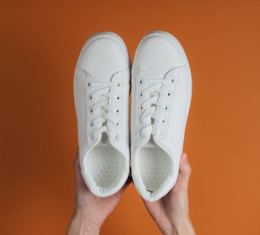 Kadın eli, kahverengi stüdyo arka planında beyaz şık ayakkabılar tutar. Üst görünüm.