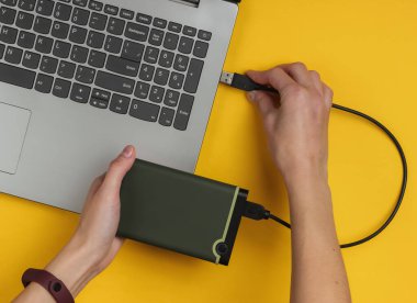 Kadın eli, sarı kağıttan bir dizüstü bilgisayara bağlanıyor. Üst görünüm