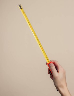 Kadın eli, sarı pastel arka planda endüstriyel mezura ile ölçümler yapar.