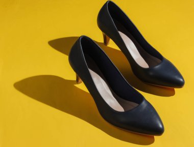Sarı kağıttan arka planda klasik yüksek topuklu kadın ayakkabıları. Şık ayakkabılar. Stüdyo çekimi. Minimalist moda natürmort.