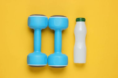 Minimalist diyet ve spor konsepti. Dambıllar, sarı kağıtta bir şişe yoğurt. Üst görünüm