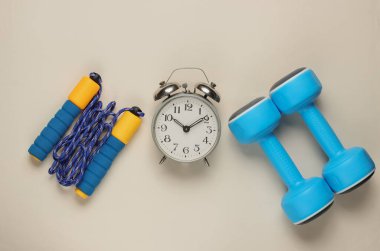 Eğitim zamanı! Dambıllar, ip atlama, beyaz arka planda çalar saat. Minimalist spor konsepti. Üst görünüm