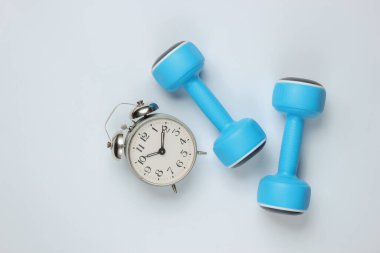 Eğitim zamanı! Dumbbell, beyaz arka planda çalar saat. Minimalist spor konsepti. Üst görünüm