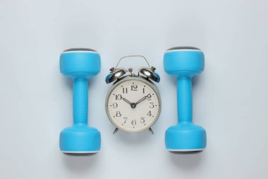 Eğitim zamanı! Dumbbell, beyaz arka planda çalar saat. Minimalist spor konsepti. Üst görünüm