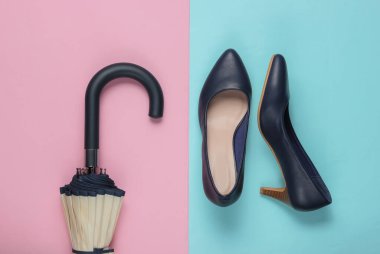 Klasik yüksek topuklu ayakkabılar, pembe mavi arka planda şemsiye. Minimalizm moda kavramı. Üst görünüm