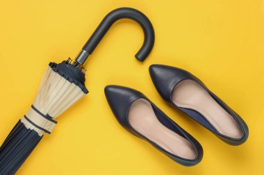 Klasik yüksek topuklu ayakkabılar, sarı arka planda şemsiye. Minimalizm moda kavramı. Üst görünüm