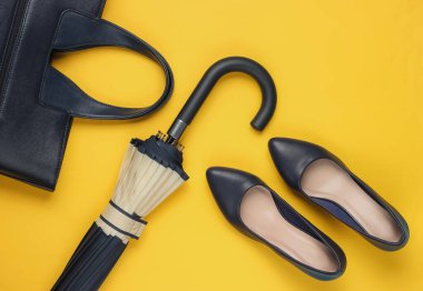 Klasik yüksek topuklu ayakkabı, deri çanta, sarı arka planda şemsiye. Minimalizm moda kavramı. Üst görünüm