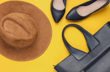 Keçeli şapka, yüksek topuklu ayakkabılar, sarı arka planda deri çanta. Minimalist moda konsepti. Üst görünüm