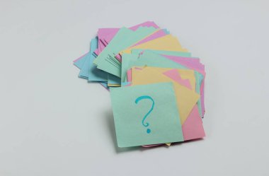 Minimalist ofis kavramı. Beyaz arka planda soru işareti olan bir sürü not kağıdı. Üst görünüm