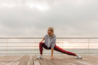 Sabah sporu. Sağlıklı yaşam tarzı kavramı. Spor giyim sektöründe genç ve çekici bir kadın gün doğumunda plajda egzersiz yapmadan önce bacak esnetiyor. Isının.