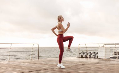 Sabah sporu. Sağlıklı yaşam tarzı kavramı. Spor giyimli genç ve çekici bir kadın güneş doğarken plajda egzersiz yapmadan önce ısınıyor. Orada koşuyor.