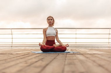Sabah açık havada yoga alıştırması yap. Spor giyim bölümündeki genç Yogi gün doğumunda plajda lotus pozisyonunda oturuyor. İç ahenk