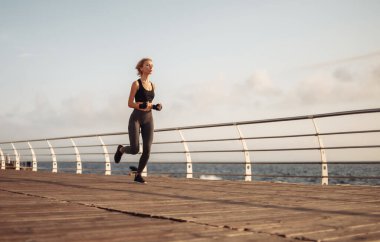 Sabah koşusu. Spor giyimli genç bir kadın güneş doğarken plajda koşuyor. Açık hava antrenmanı. Sağlıklı yaşam tarzı