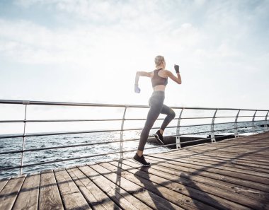 Sabah koşusu. Spor giyimli genç bir kadın güneş doğarken plajda koşuyor. Hızlı koşu. Sağlıklı bir yaşam tarzı. Arka plan