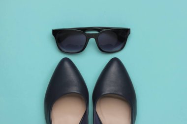 Şık bir kadın görünüşü. Deri yüksek topuklu ayakkabılar ve mavi arka planda güneş gözlüğü. Üst görünüm