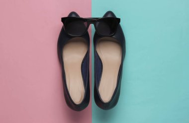 Şık bir kadın görünüşü. Deri yüksek topuklu ayakkabılar ve mavi arka planda güneş gözlüğü. Üst görünüm