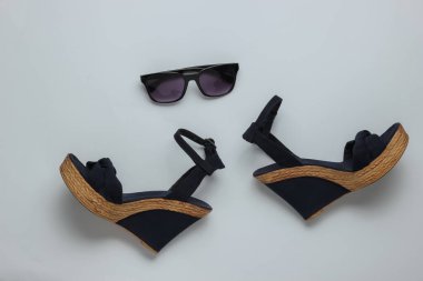 Platformlu kadın sandaletleri, beyaz arka planda güneş gözlükleri. Kadın yaz ayakkabıları ve aksesuarları. Üst görünüm.