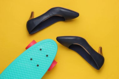 Yaz eğlencesi. Sarı stüdyo arka planında kruvazör tahtasıyla yüksek topuklu kadın ayakkabıları. Moda çekimi, üst manzara.