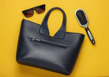 Sarı arka planda düz stil kadın aksesuarları vardı. Çanta, güneş gözlüğü, tarak. Üst görünüm