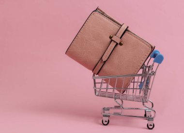 Minimalist alışveriş konsepti. Pembe pastel arka planda cüzdanı olan mini alışveriş arabası.