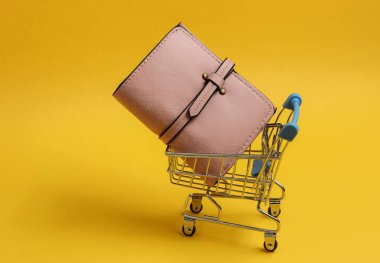 Minimalist alışveriş konsepti. Sarı arka planda cüzdanı olan küçük bir alışveriş arabası.