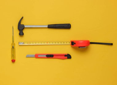 Çekiç, tornavida, sarı arka planda bıçak ve cetvel. Üst görünüm, minimalizm