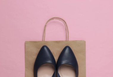 Alışveriş konsepti. Moda stüdyosu çekimi. Pembe pastel arka planda alışveriş yapmak için yüksek topuklu ayakkabılar ve kese kağıdı. Üst görünüm