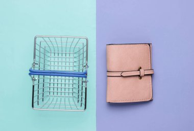 Minimalist alışveriş konsepti. Mini alışveriş sepeti ve mor arka planda deri cüzdan. Üst görünüm