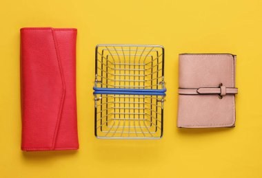 Minimalist alışveriş konsepti. Mini alışveriş sepeti ve sarı arka planda iki cüzdan. Üst görünüm