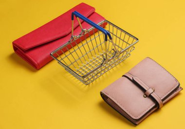Minimalist alışveriş konsepti. Mini alışveriş sepeti ve sarı arka planda iki cüzdan.