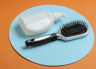 Minimalist güzellik konsepti. Saç bakımı. Kahverengi arka planda mavi halkalı tarak ve bir şişe şampuan..