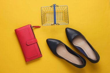 Alışveriş konsepti. Moda stüdyosu çekimi. Yüksek topuklu ayakkabılar, alışveriş sepeti, sarı arka planda cüzdan. Üst görünüm