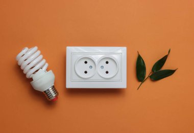 Eko konsepti. Güç Enerji Ekonomisi. Gezegeni kurtar. Çift güç prizi, yeşil yapraklar, kahverengi arka planda spiral lamba. Stüdyo çekimi