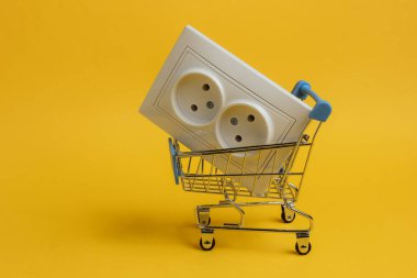 Sarı arka planda çifte elektrik prizi olan alışveriş arabası.