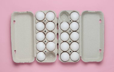 Üzerinde pembe pastel arka planda yumurtalar olan karton tepsiler. Minimalizm aşçılık konsepti. Üst görünüm.