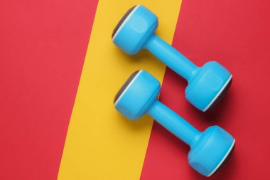 Kırmızı-sarı bir arka planda plastik halterler. Minimalizm fitness konsepti. Üst görünüm