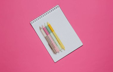Pembe arka planda bir sürü renkli kalem ve defter yakın plan..