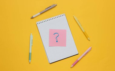 Kalemli not defteri ve sarı arka planda soru işareti olan not defteri. Üst görünüm