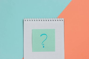 Pembe mavi arkaplanda soru işareti olan not defteri ve not kağıdı..