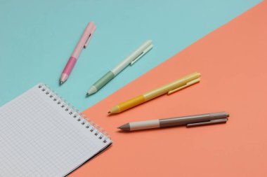 Bir sürü renkli kalem ve mavi pembe arkaplan üzerine yakın plan defter..