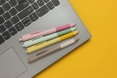 Laptop ve sarı arka planda bir sürü renkli kalem. Üst görünüm