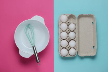 Yemek pişirme konsepti. Boş beyaz kase çırpılmış, pembe mavi stüdyo arka planında yumurta tepsisi. Üst görünüm.