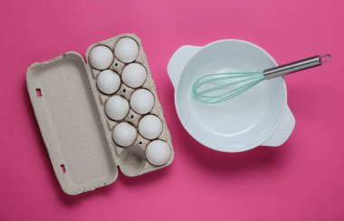 Yemek pişirme konsepti. Boş beyaz kase çırpılmış, pembe stüdyo arka planında yumurta tepsisi. Üst görünüm.