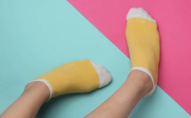 Pembe mavi stüdyo arka planında sarı çoraplı kadın bacakları. Pastel renk eğilimi. Minimalist moda konsepti. Üst görünüm