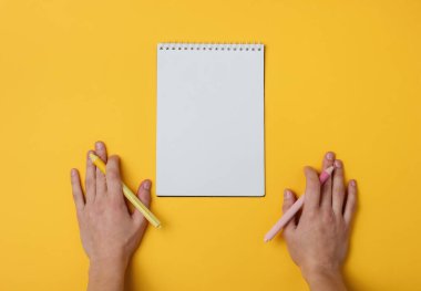 Ambidextr, sarı arka planda kalem ve defter olan iki kadın eli. Kızın günlüğü. Üst görünüm