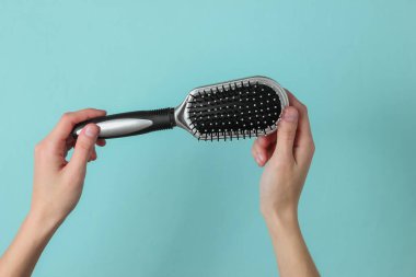 Kadın elleri mavi arka planda tarak tutuyor. Saç bakımı. Güzellik konsepti