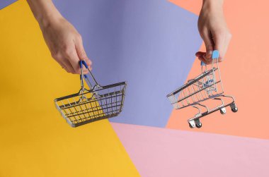 Alışveriş konsepti. Kadın eli renkli arka planda mini alışveriş sepeti ve tramvay tutuyor. Minimalizm